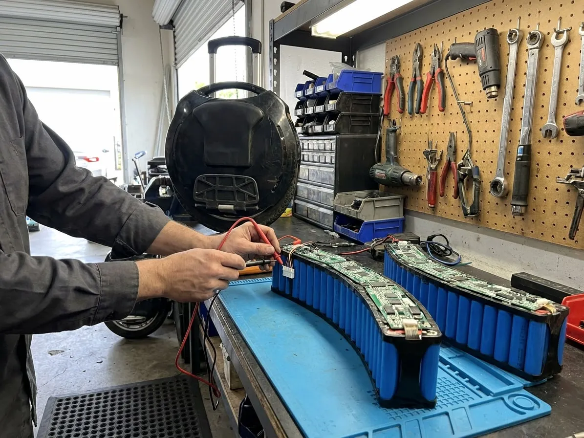 Technician measuring the balance connector of a curved electric unicycle battery pack with multimeter probes