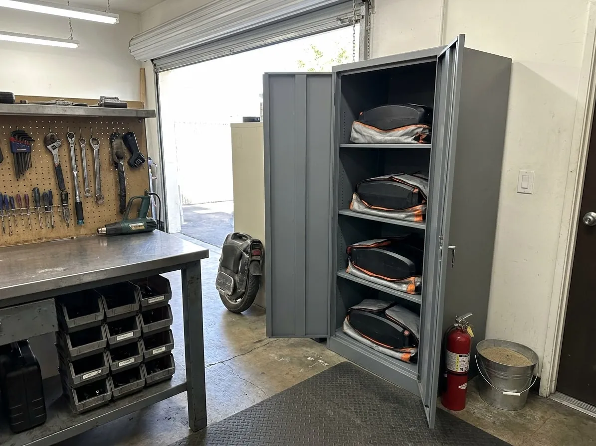 Steel fire-resistant cabinet holding electric unicycle battery packs in fire-resistant bags, with an extinguisher beside it