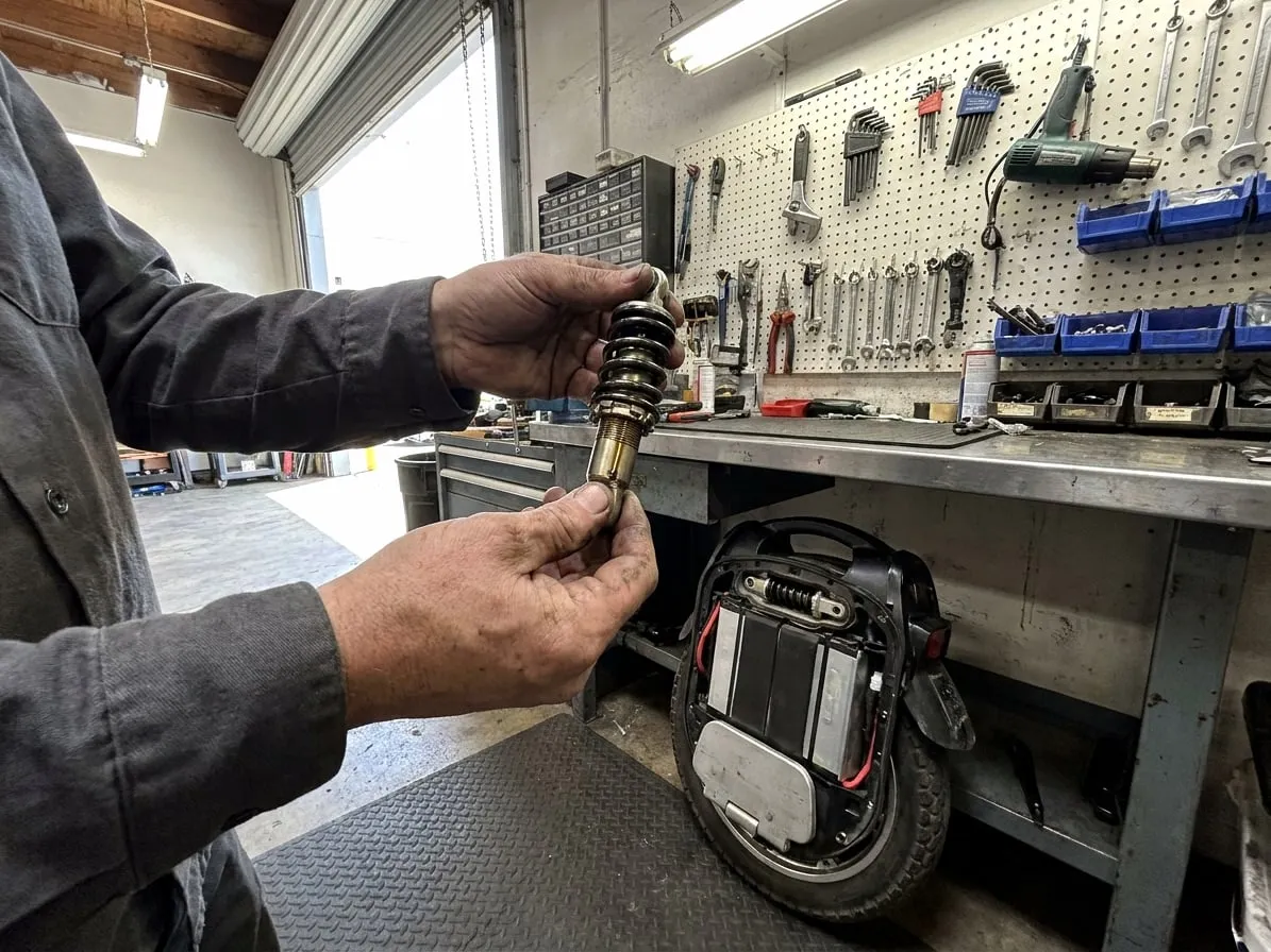 Technician inspecting a coil-over shock removed from an electric unicycle suspension