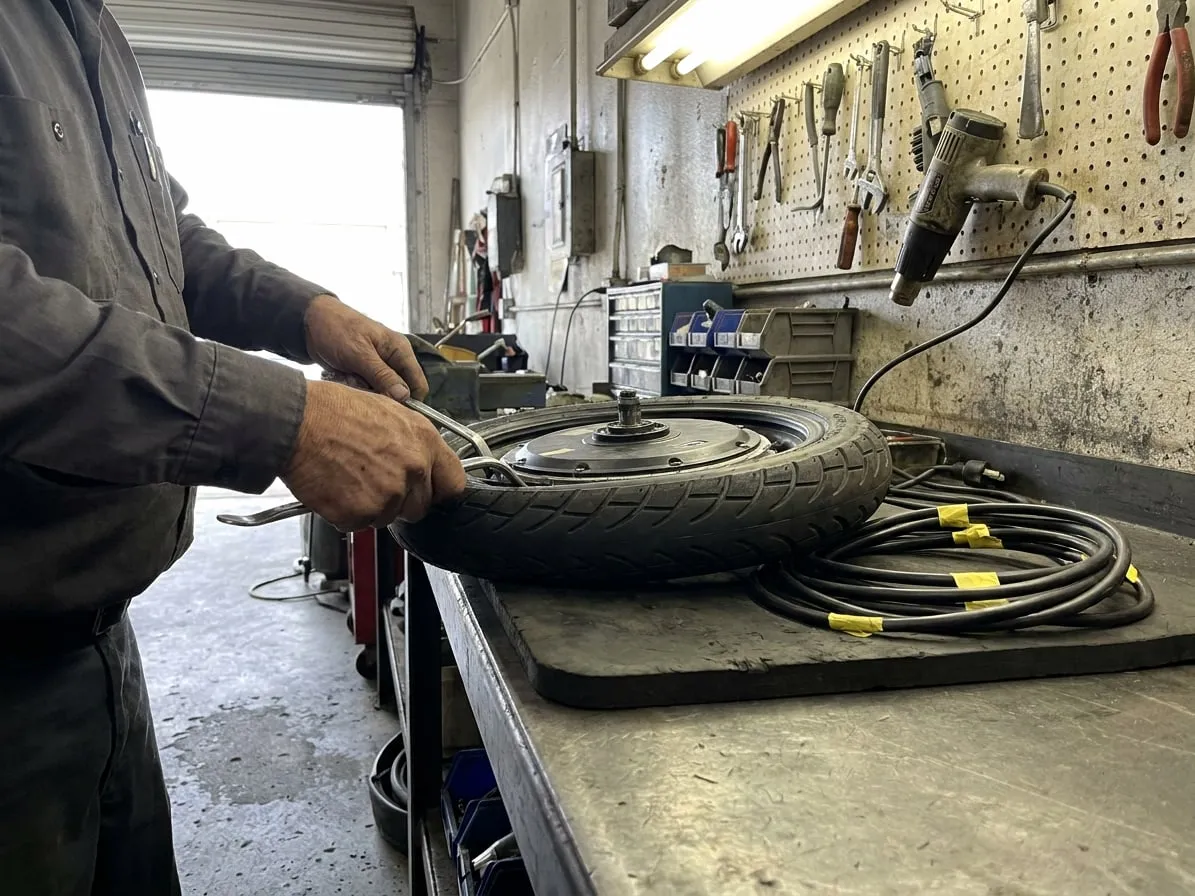 Technician levering a tire off the hub motor of an electric unicycle with two motorcycle tire spoons